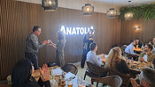 Das Bild zeigt Personen an Tischen im Saal des Restaurants Anatolia. Eine Person überreicht einer anderen Person eine Tasse.