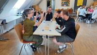 Das Bild zeigt eine Gruppe Anwärter*innen des Studienseminars für BBS Neuwied in einem Raum beim Erleben des Spiels Kulturralley . Dabei sitzen sie in Gruppen an Tischen.