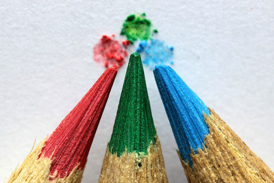 Das Bild zeigt in Nahaufnahme die Spitzen dreier Buntstifte, die zentriert in die Mitte des Bildes zeigen. Die Farben sind von links nach rechts rot, grün und blau.