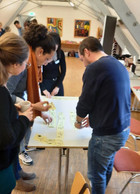 An einem Tisch beschreiben stehend die Teilnehmer:innen mit Hilfe von Visualisierungen auf Post-its einen Prozess (Tool: Magic-System-Mapping)